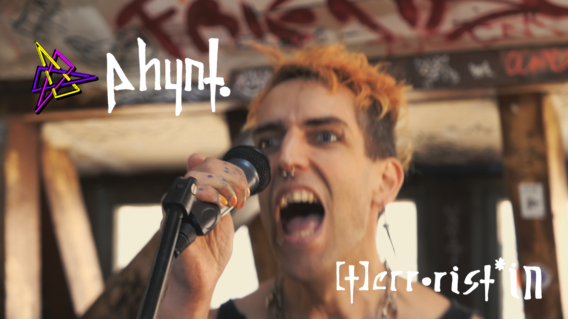 Screenshot aus dem Musikvideo zu [T]errorist*in: ph4nt. am Mikro, schreiend und mit orangenen Haaren. Nahaufnahme. Hintergrund sieht nach AZ aus.
