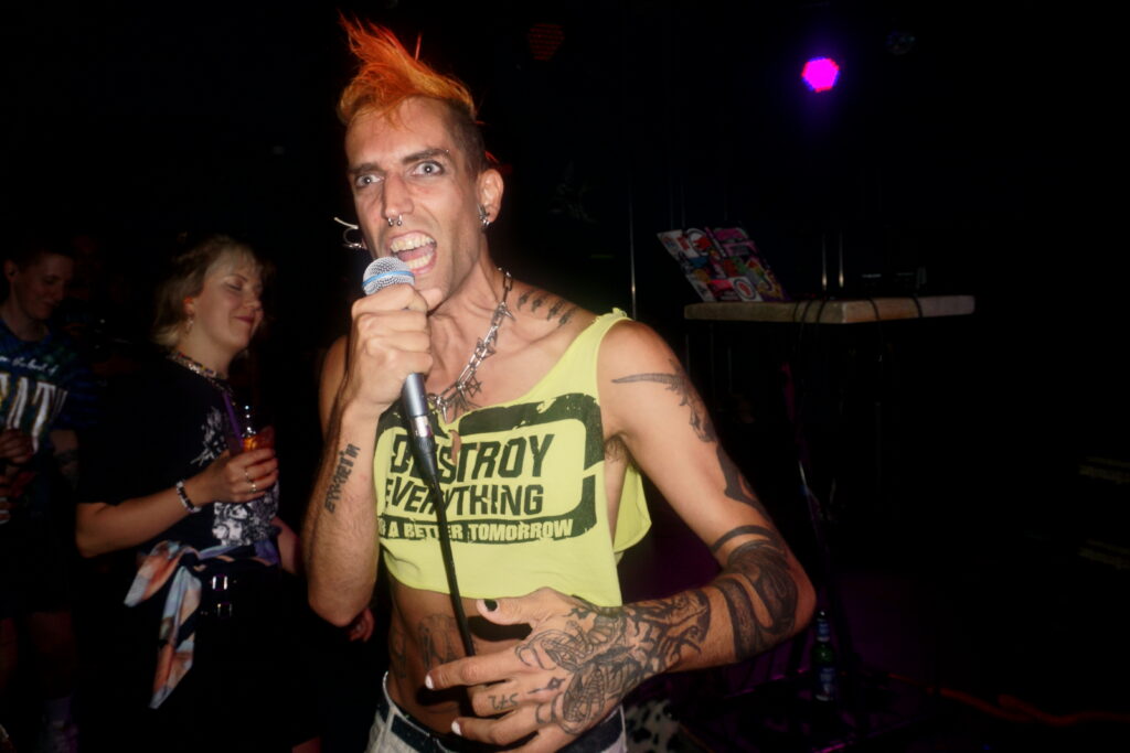 ph4nt mit orangenem Iro & neongrünem "Destroy Everything for a better Tomorrow"-Croptop schreit in's Mikro, inmitten des Publikums. Sehr punkig :D